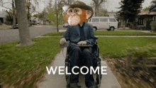 a man in a suit and cowboy hat is sitting in a wheelchair with welcome written on the sidewalk behind him