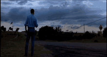 a man in a blue shirt is standing on the side of a road in front of a road sign