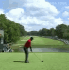 a man in a red shirt is swinging a golf club at a golf ball on a golf course .