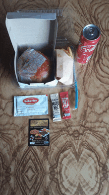 a can of coca cola sits next to a box of hamburgers and condiments