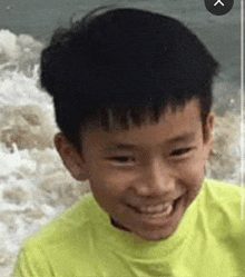 a young boy wearing a yellow shirt is smiling in front of the ocean .