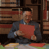 a man in a striped suit holds a red piece of paper in front of a bookshelf that has arsenal on it