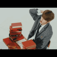 a man in a suit and tie is sitting at a desk with a stack of red books on it .