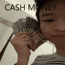 a young man is holding a fan of money in front of his face with the words cash money written above him