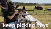 a man sitting at a picnic table holding a rifle with the words " keep picking boys " written below him