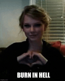 a woman is making a heart shape with her hands while sitting on a couch .