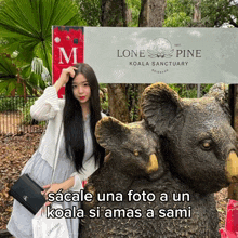 a woman stands next to a statue of a koala bear in front of a sign for the lone pine koala sanctuary