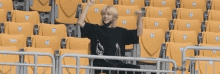 a man in a black shirt is sitting in an empty stadium with his arms in the air