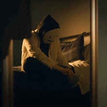 a person wearing a mask sits on a bed in a dark room