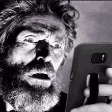 a black and white photo of a man with a beard looking at a cell phone