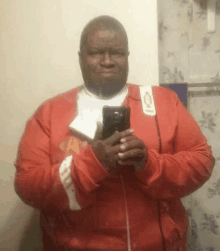 a man in a red jacket is taking a selfie with his cell phone .