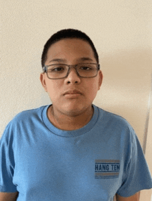 a boy wearing glasses and a blue shirt that says hang ten on it