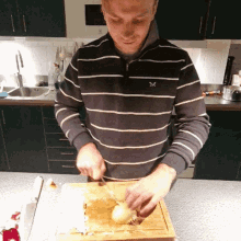 a man in a striped shirt with a x on his chest is cutting an onion on a wooden cutting board