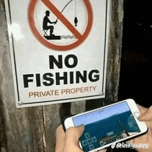 a person is holding a phone in front of a sign that says no fishing