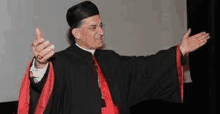 a man in a black robe and red cape is standing with his arms outstretched in front of a screen .