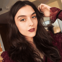 a woman wearing a maroon lace top takes a selfie