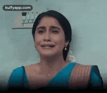 a woman in a blue saree is crying while standing in front of a wall .