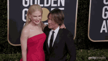 a woman in a red dress and a man in a black suit are posing for a picture on the red carpet at the golden globes