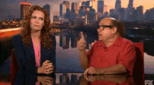 a man in a red shirt is talking to a woman in a pink shirt in front of a city skyline