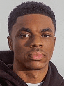 a close up of a young man 's face wearing a black hoodie and a white shirt .