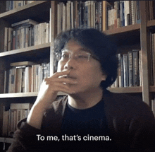 a man sitting in front of a bookshelf with the words to me that 's cinema below him