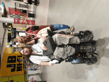 a man in a wheelchair standing next to a woman in front of a jb hi-fi sign