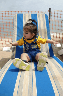 a little girl wearing overalls and a yellow shirt with the letter s on it sits on a beach chair