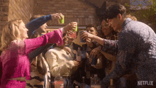 a group of people toasting with drinks in front of a brick wall with a netflix logo in the corner