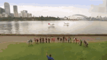 a group of people are standing on a field in front of a body of water with the sydney opera house in the background