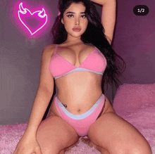 a woman in a pink bra and panties is kneeling on a bed with a neon heart behind her