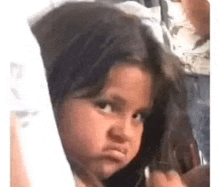 a little girl with long hair is making a funny face while looking at the camera .