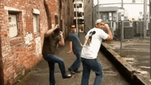 three men are dancing on a sidewalk in front of a brick building with a sign that says dance on it