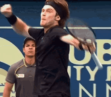 a man in a black shirt is holding a tennis racquet in front of a sign that says u.s. open