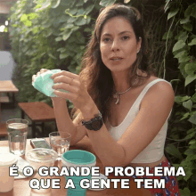 a woman sitting at a table holding a cup with the words " e o grande problema que a gente tem " below her