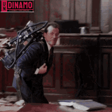 a man in a suit and tie is carrying a camera on his back and the word dinamo is above him