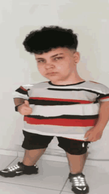 a young boy wearing a striped shirt and shorts is giving a thumbs up sign