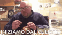 a bald man with glasses is sitting at a table eating food with the words " iniziamo dal culetto " written above him