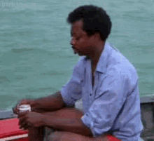 a man in a blue shirt is sitting on a boat with a can of soda in his hand .