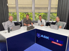 four men sit at a table in front of a sign that says askblue podcast