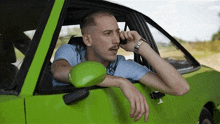 a man with a mustache is talking on a cell phone in a green car .