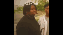 a man in a black shirt is standing next to another man in a white shirt with the word alt + tab on it .