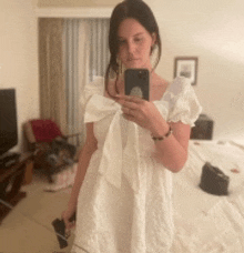 a woman in a white dress is taking a picture of herself in the mirror