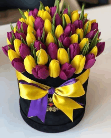 a box filled with yellow and purple tulips with a purple bow