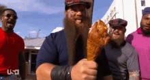 a man with a beard is holding a chicken leg in front of a group of men with usa written on their shirts