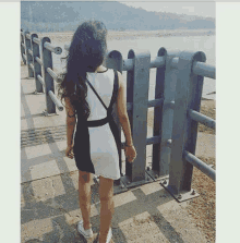 a woman in a black and white dress is standing next to a fence and looking at the water .