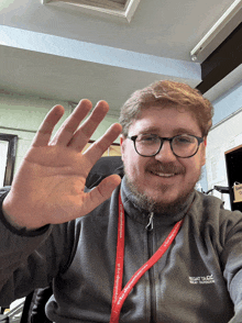 a man wearing glasses and a grey regatta jacket waves