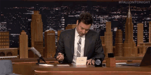 a man in a suit and tie is sitting at a desk writing a note on a piece of paper .