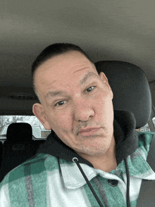 a man in a green plaid shirt is sitting in a car