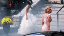 a woman in a wedding dress is walking down the stairs next to a woman in a pink dress .