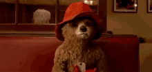 a teddy bear wearing a red hat is sitting on a red bench holding a cup of tea .